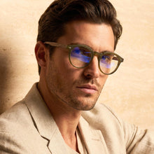 Man wearing round green reading  glasses with a neutral background