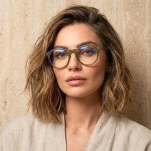 Woman wearing green round readers' glasses with a neutral background